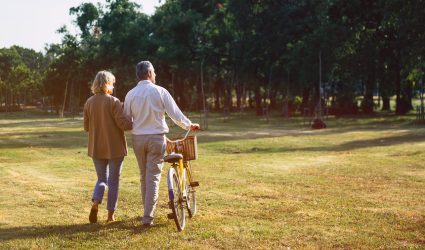 The behind of Caucasian elderly couples walking with a bicycle in the natural autumn sunlight garden feel cherish and love, concept elderly love, warm family, happy retirement, retirement lifestyle.