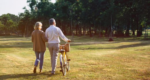 The behind of Caucasian elderly couples walking with a bicycle in the natural autumn sunlight garden feel cherish and love, concept elderly love, warm family, happy retirement, retirement lifestyle.