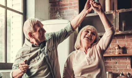 Beautiful senior couple is dancing and smiling while cooking together in kitchen
