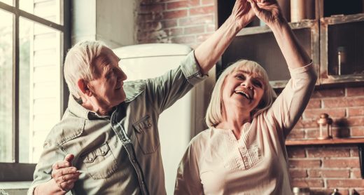 Beautiful senior couple is dancing and smiling while cooking together in kitchen